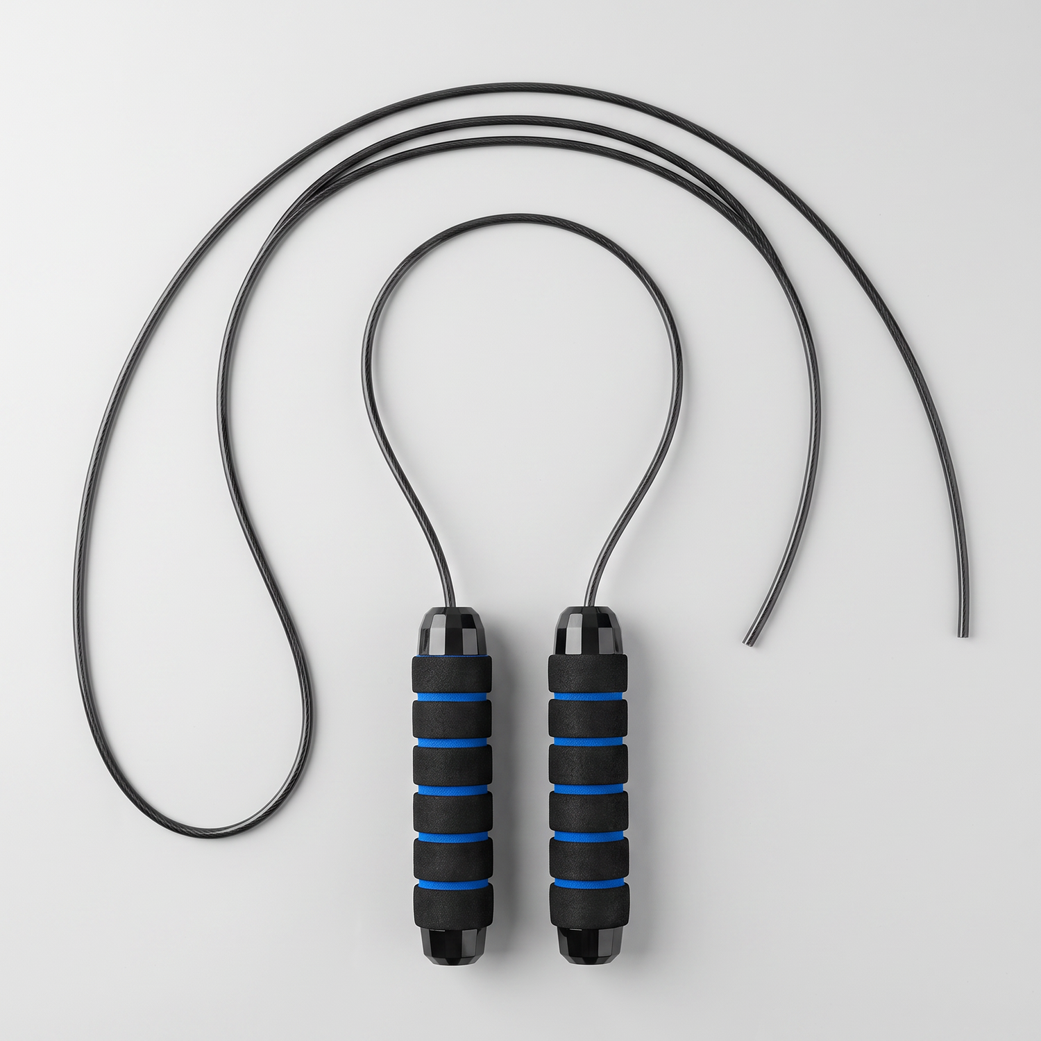 Corde à sauter dépliée à plat, câble noir déroulé et deux poignées mousse à anneaux bleus