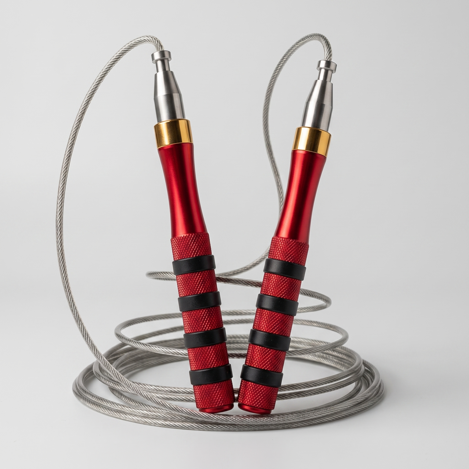 Corde à sauter speed rope aux poignées en aluminium rouge et câble acier, posée sur fond gris clair