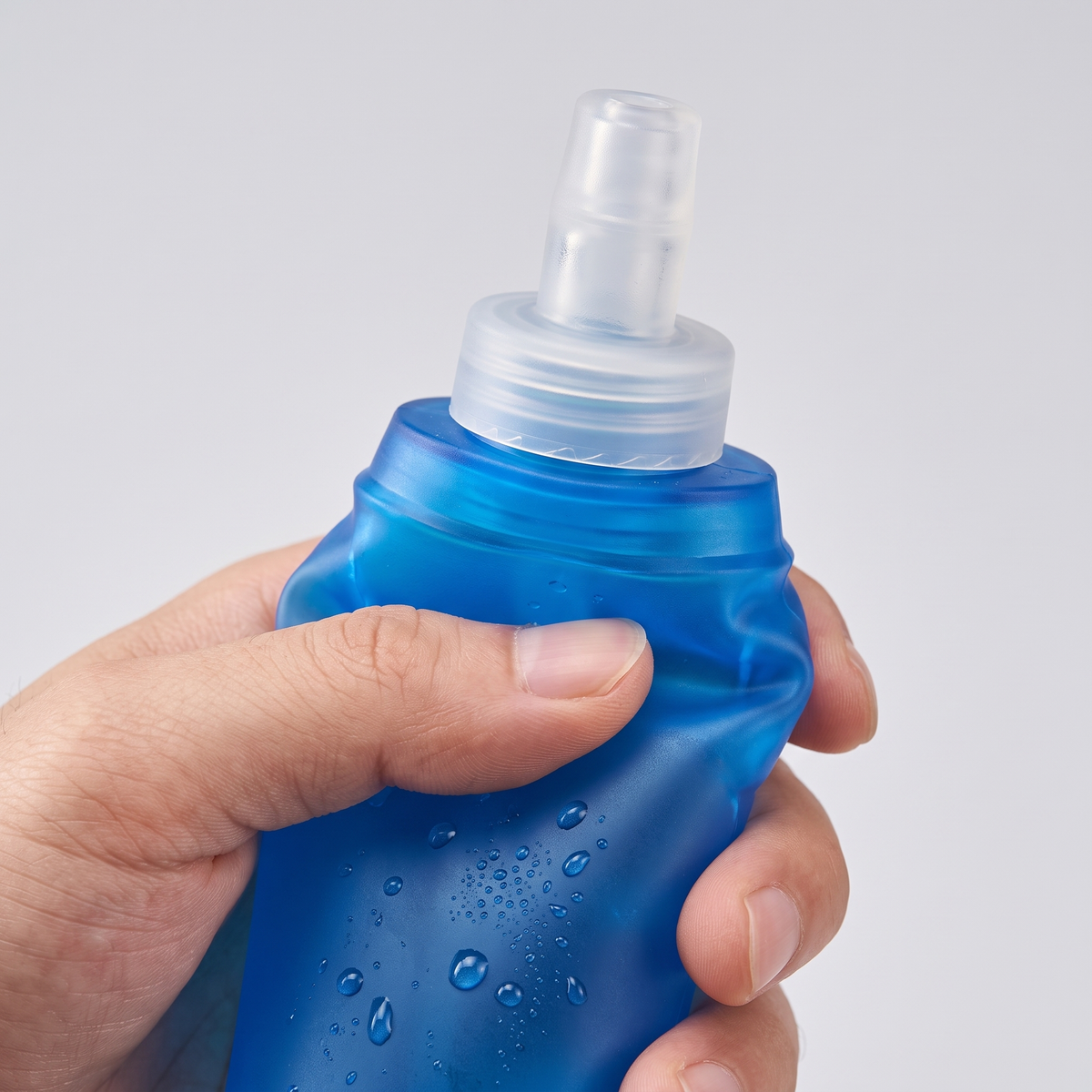 Main qui presse la flasque souple bleue : gros plan sur le bouchon et la valve à mordre