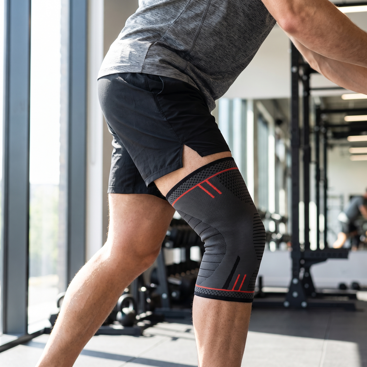 Genouillère de compression sangle rotule noire et rouge portée en salle de sport